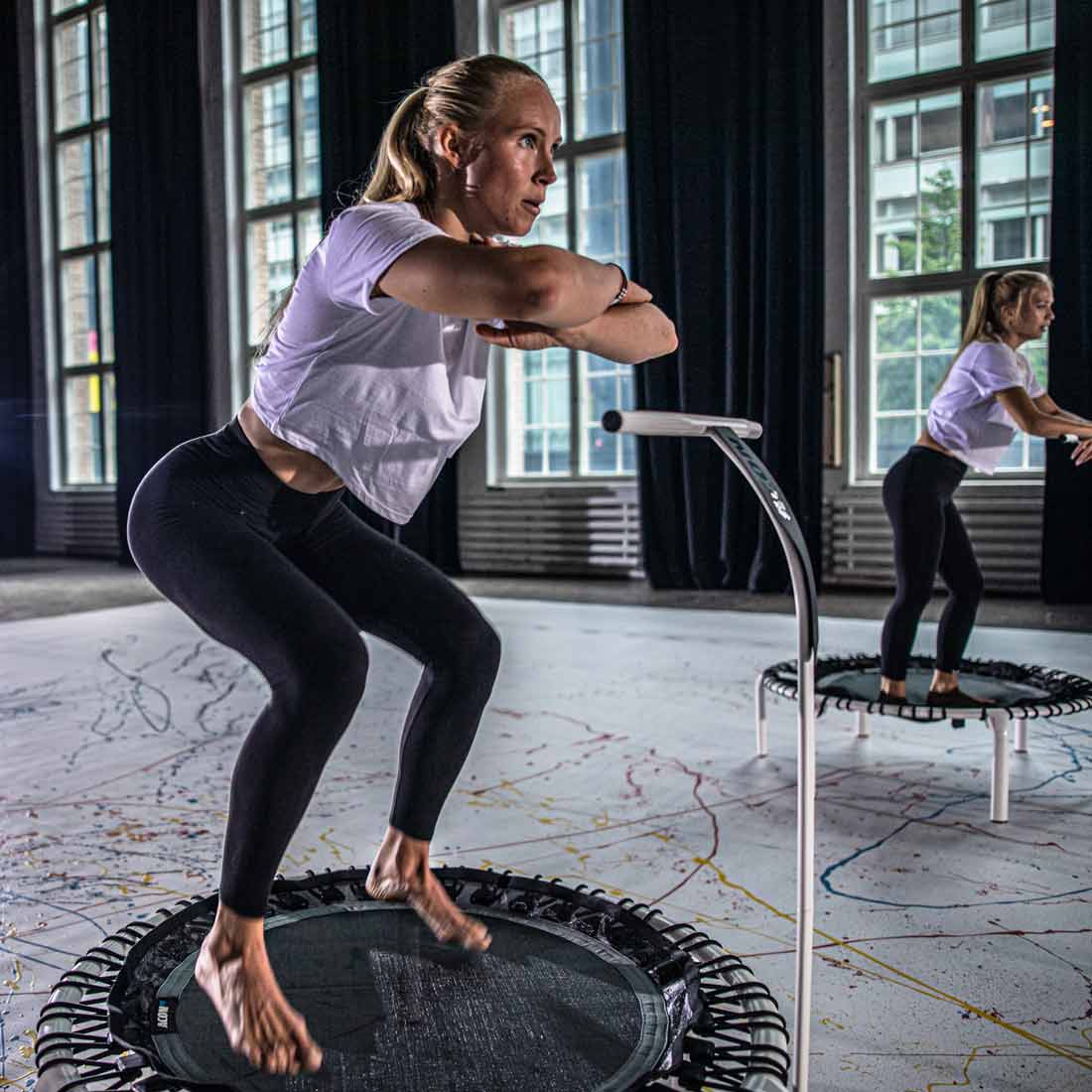 Mulheres a saltar em mini trampolins num ginásio interior com janelas grandes.