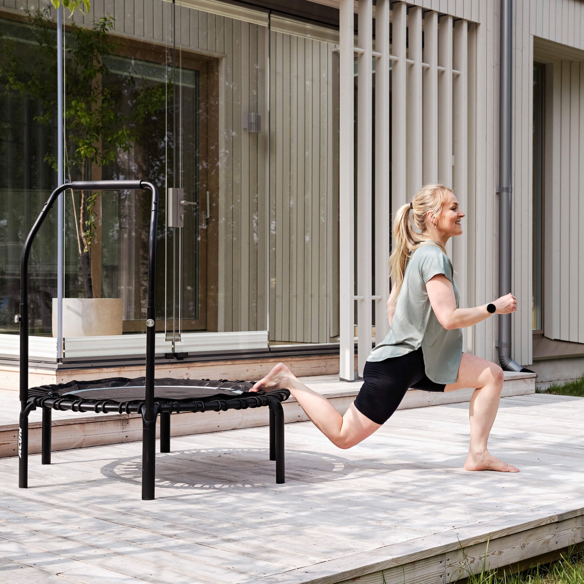 Mini trampolim preto de fitness exterior com mulher a fazer exercício ao lado