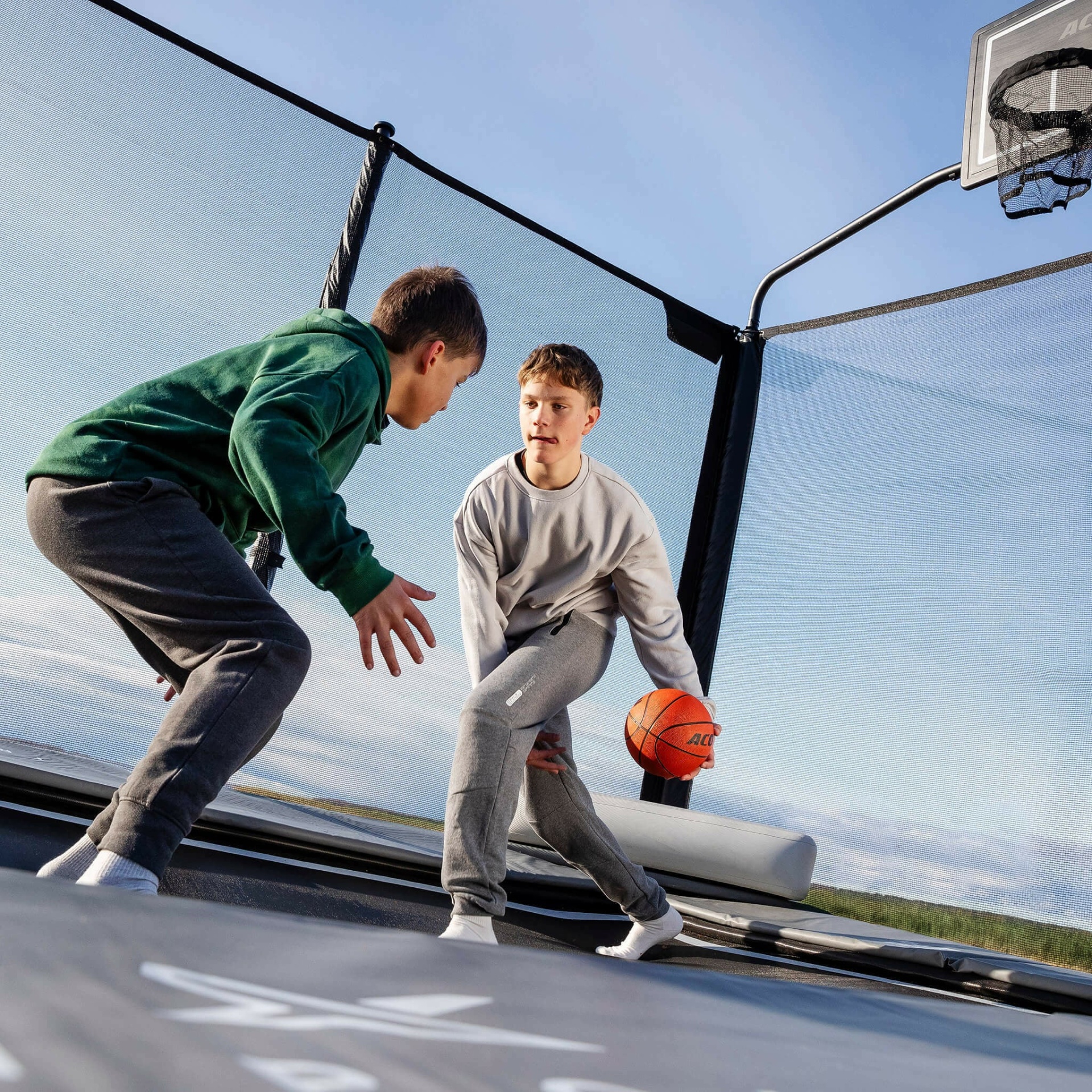 Trampolim com rede de proteção e painel de basquetebol ao ar livre com crianças a jogar basquetebol.