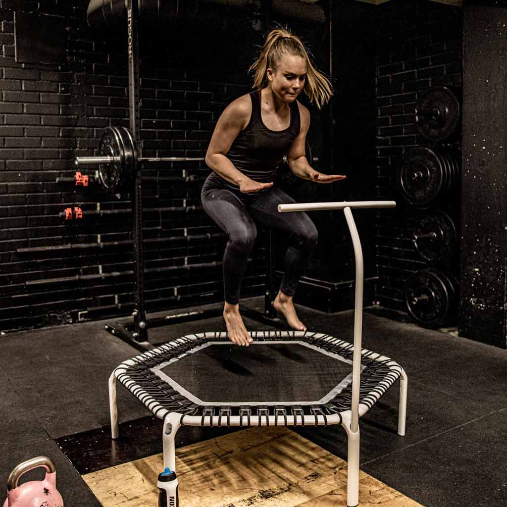 Mulher a saltar num trampolim branco com pega num ginásio