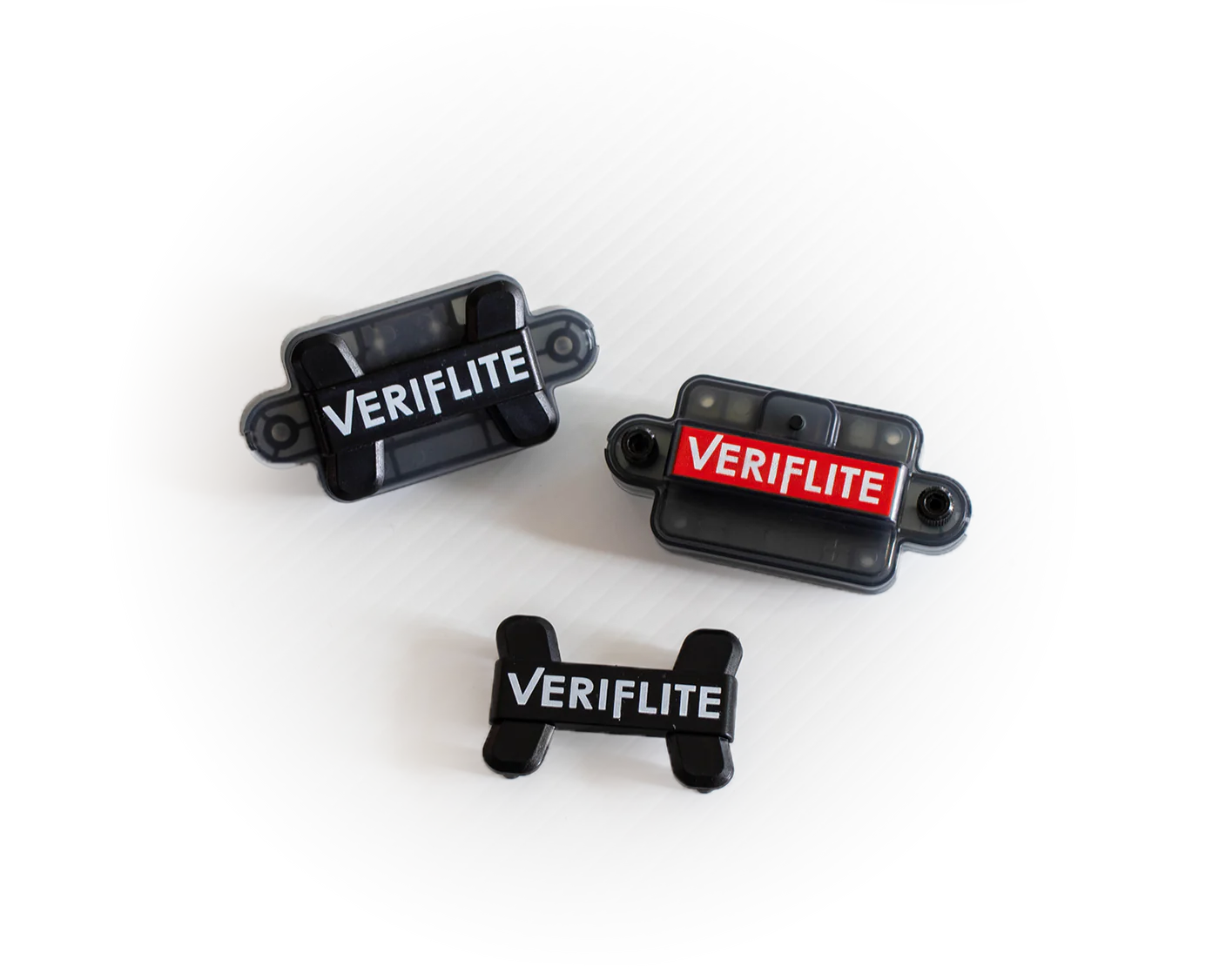 Três dispositivos eletrónicos pequenos pretos com rótulos VERIFLITE posados em superfície branca texturizada.
