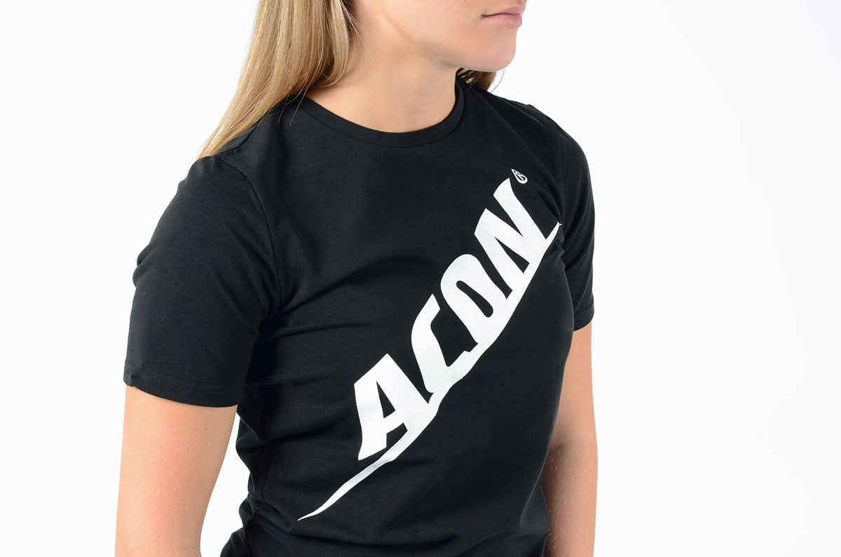 T-shirt preta com texto branco diagonal ACÔN usada por mulher com cabelo loiro