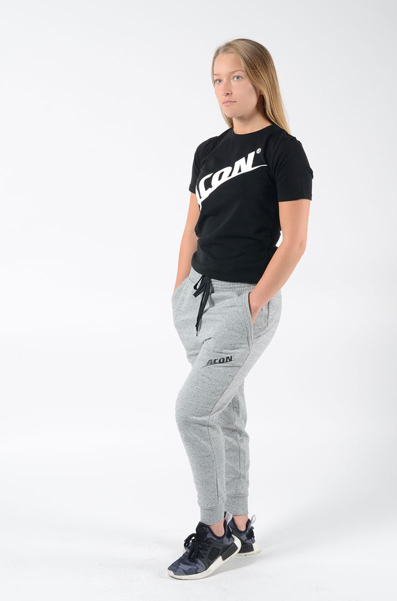 Mulher com camisola preta ACON, calças cinza e ténis pretos