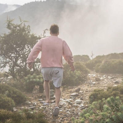 Homem de sweatshirt rosa e calções cinza a caminhar numa trilha de montanha
