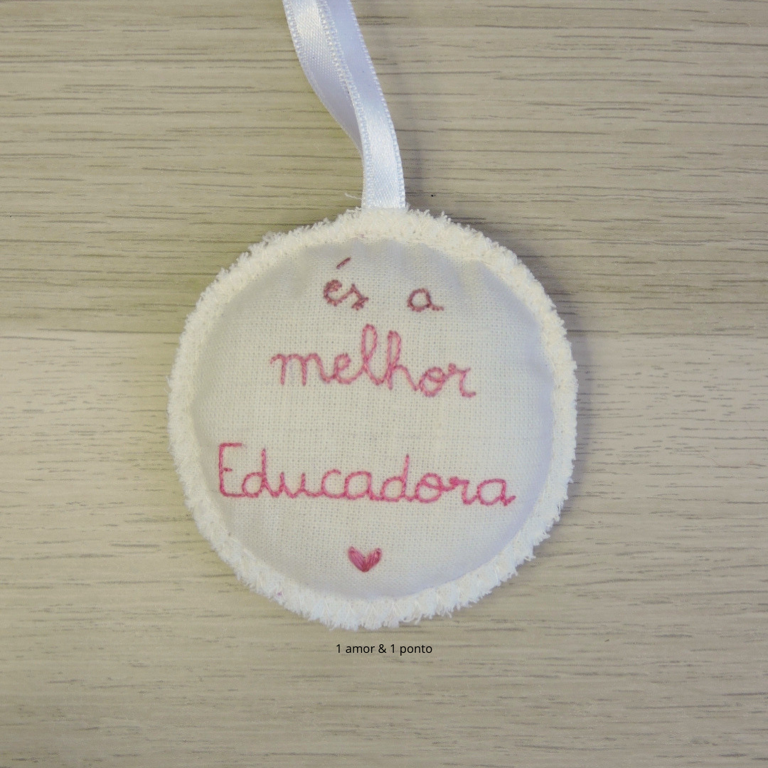 Ornamento de tecido branco bordado com mensagem para educadora e fita para pendurar