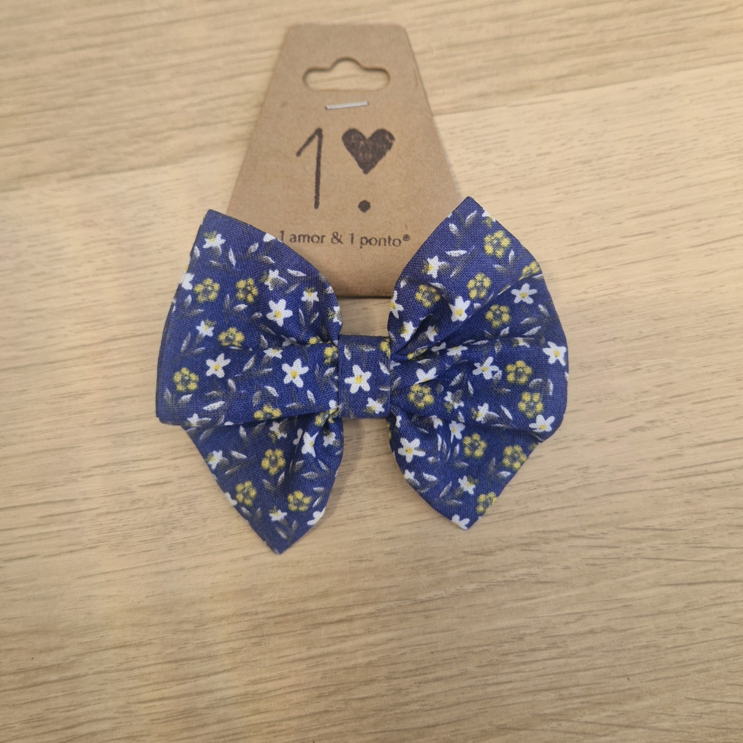 Laço tecido azul com flores brancas e amarelas em cartão castanho sobre madeira clara