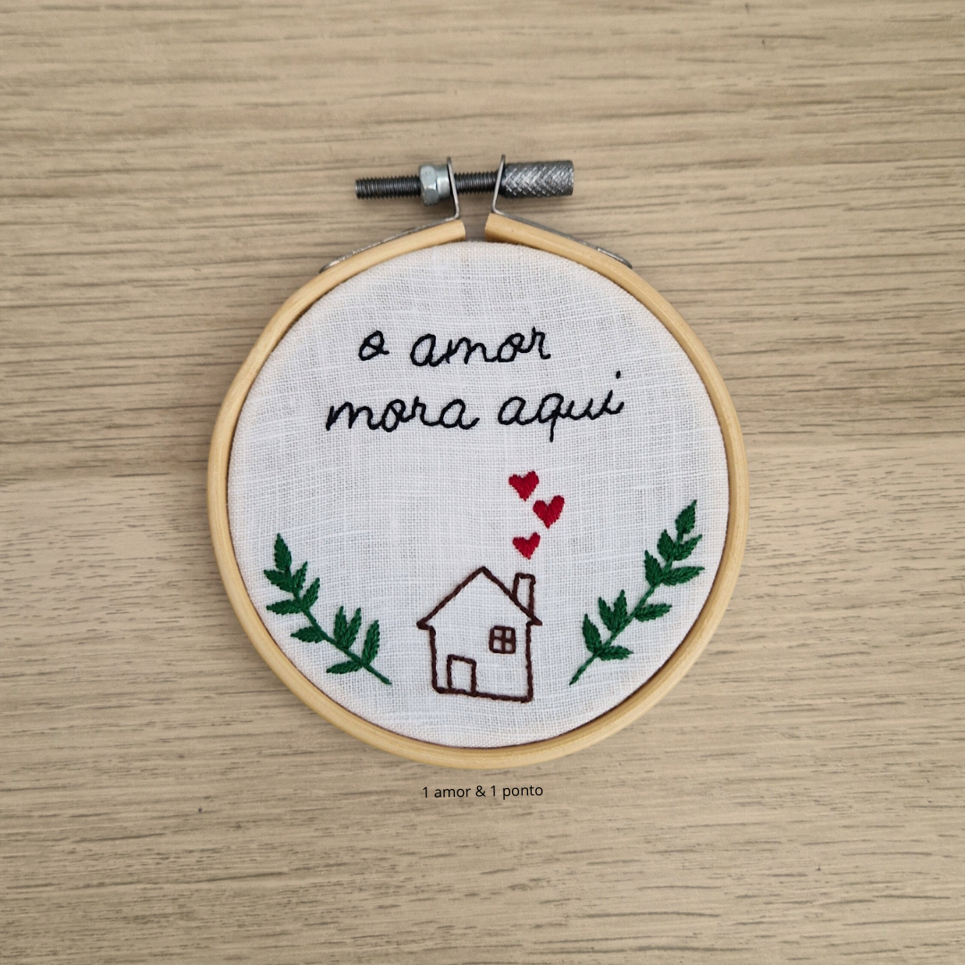 Bordado com frase e desenho em bastidor de madeira sobre madeira clara.