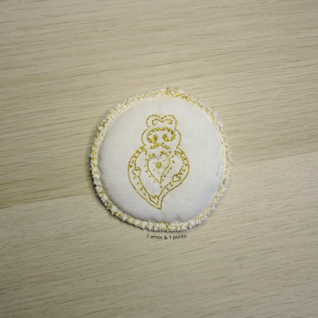 Alfineteiro redondo branco com bordado dourado sobre superfície de madeira clara