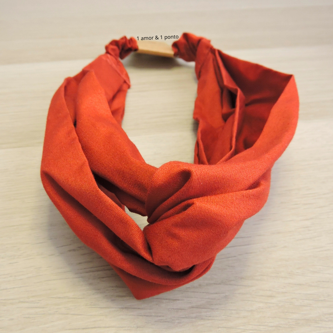 Faixa de cabelo em tecido laranja com parte torcida e elástico
