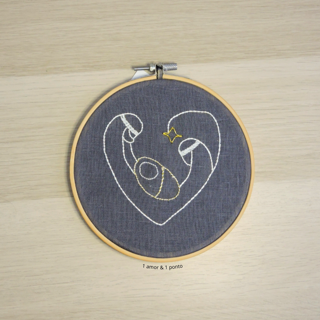 Bordado em bastidor de madeira com desenho abstrato em forma de coração no tecido cinza escuro