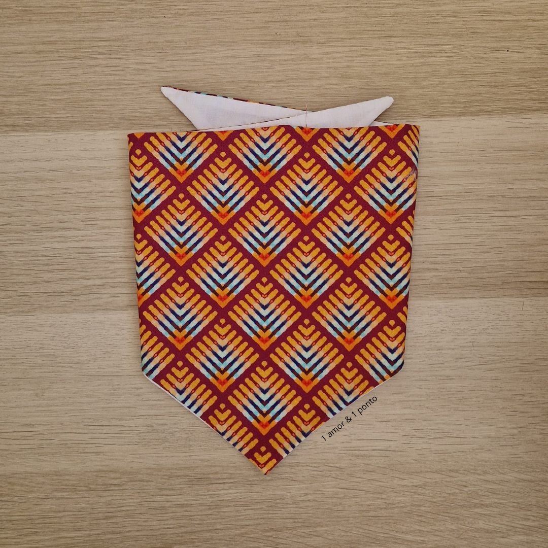 Bandana triangular com padrão geométrico colorido sobre fundo de madeira