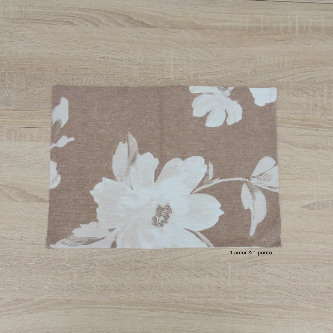 Tecido quadrado castanho com flores brancas e bege sobre madeira clara.
