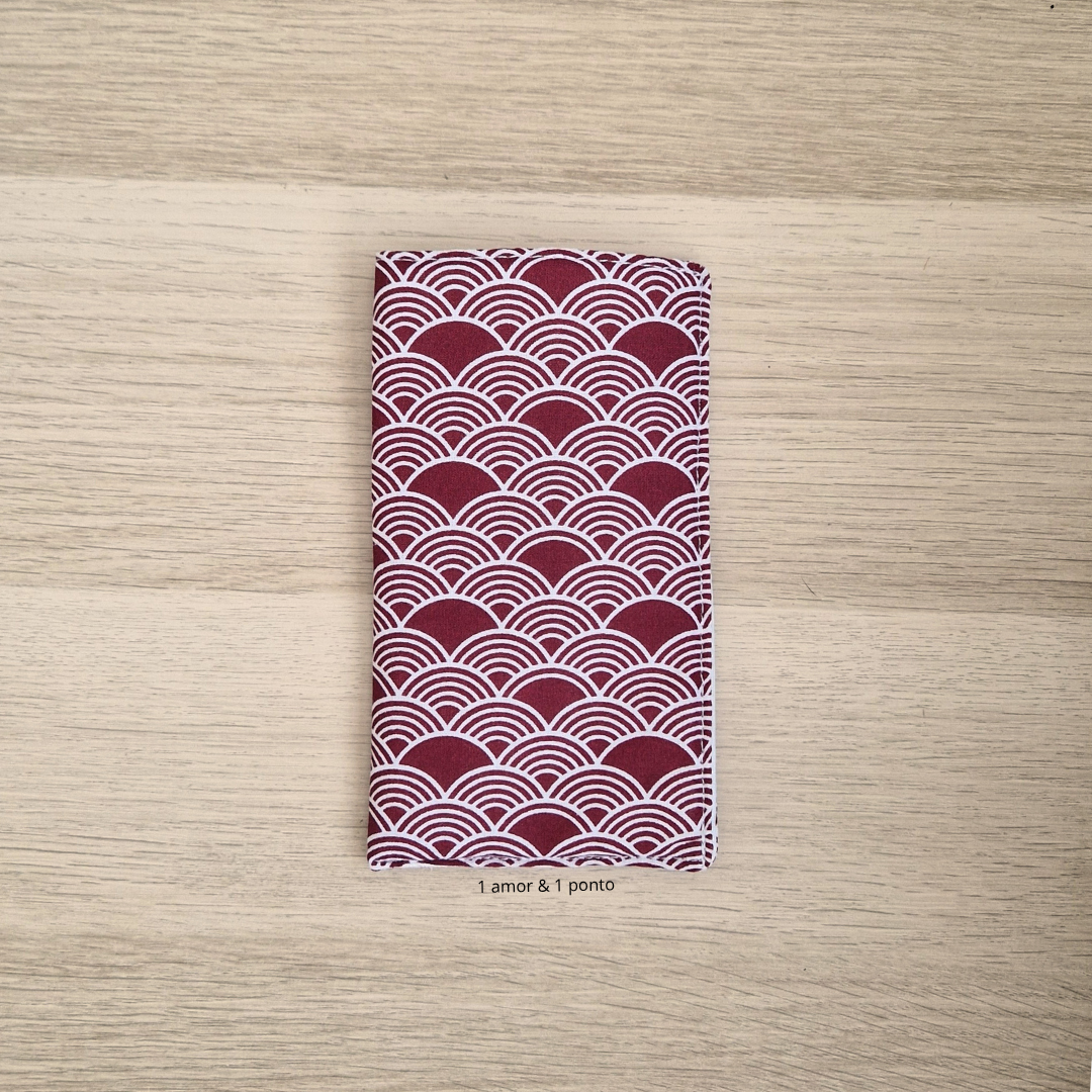 Carteira ou porta-cartões com padrão de ondas vermelho e branco sobre mesa de madeira clara