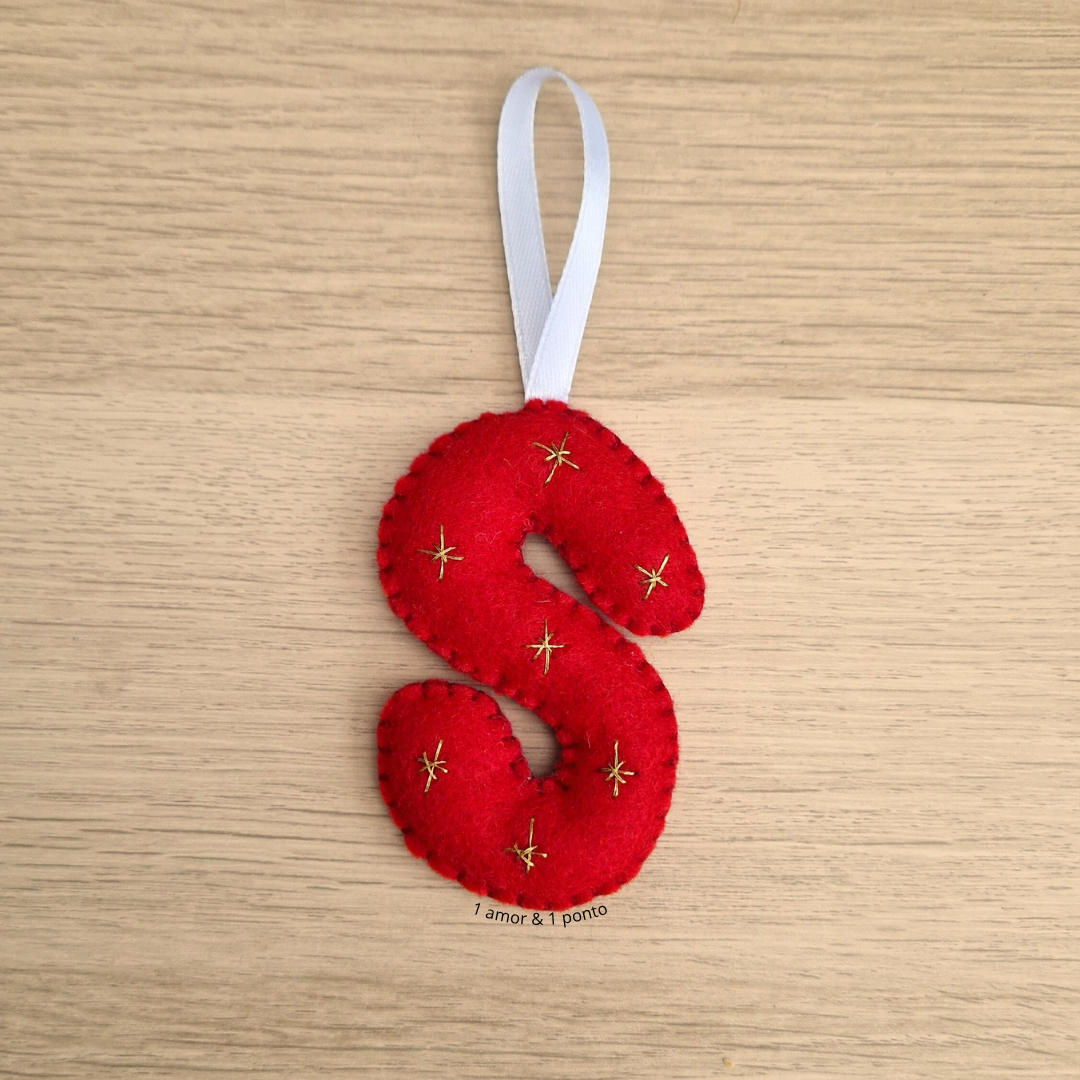 Enfeite em feltro vermelho formato letra S com estrelas douradas e fita branca para pendurar