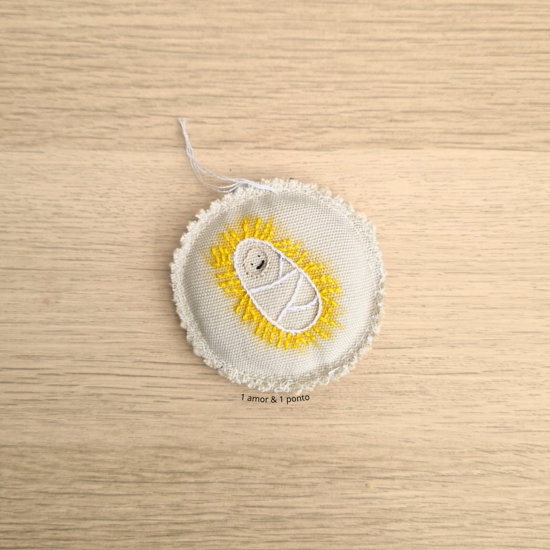 Patch bordado redondo com bebé em manta branca e detalhes amarelos