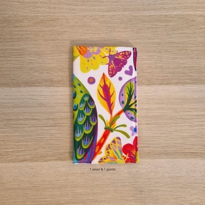 Carteira de tecido colorida com padrão de folhas e borboletas sobre fundo claro.