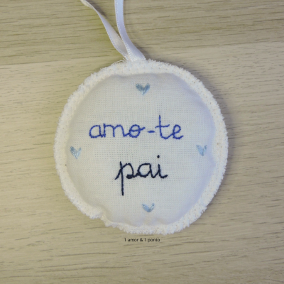 Ornamento de tecido branco com bordado azul e preto 