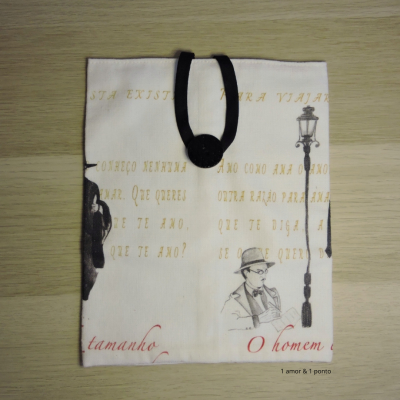 Estojo de tecido branco com texto em português e ilustrações em preto e amarelo, com fecho de fita preta e botão.