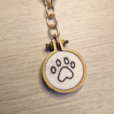 Chaveiro de madeira com bordado de pata preta em tecido branco