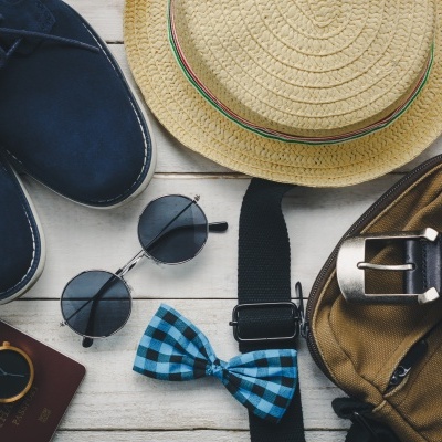 Sapatos, chapéu de palha, óculos escuros, gravata borboleta, relógio, cinto e mochila sobre madeira clara