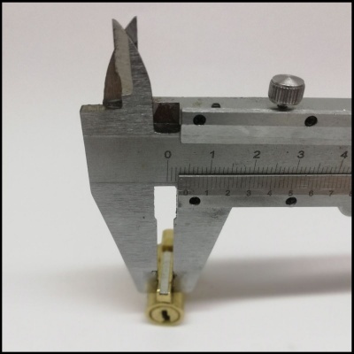 Paquímetro metálico a medir um pequeno objecto amarelo cilíndrico