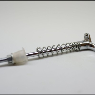 Peça metálica com mola espiral e peça plástica translúcida sobre superfície branca