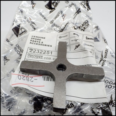 Peça metálica em forma de cruz sobre embalagem com etiquetas e texto