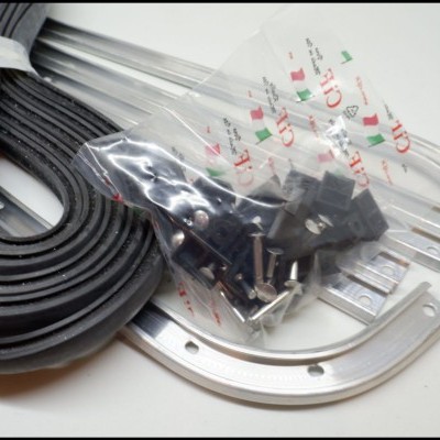 Conjunto de vedação em borracha preta, calhas metálicas cinzentas e saco com parafusos sobre fundo branco