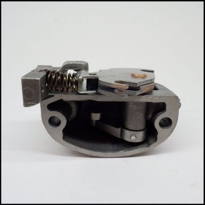 Componente mecânico metálico cinza com mola preta numa superfície branca