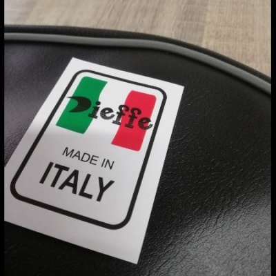 Etiqueta MADE IN ITALY sobre superfície preta texturada, borda cinza e fundo em madeira clara