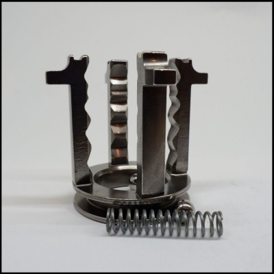 Peça metálica com quatro garras verticais e mola helicoidal prateada