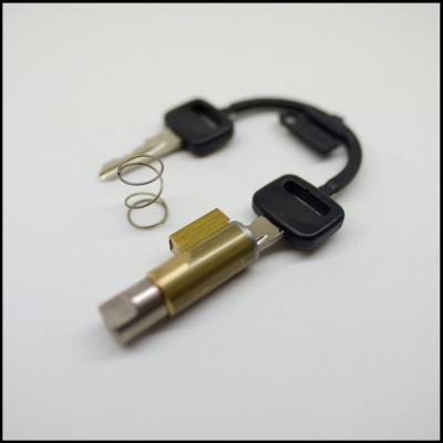 Conjunto de ferramenta para cadeados com chaves, cilindro metálico dourado e mola, fundo branco.