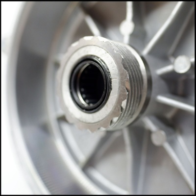 Peça metálica cilíndrica com anel preto no centro montada numa estrutura prateada com raios