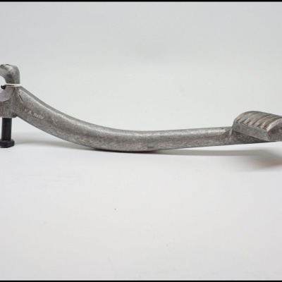 Pedal metálico cinzento com parafuso numa superfície branca