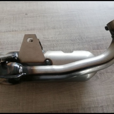 Escape de moto em metal prateado e preto sobre superfície de madeira clara