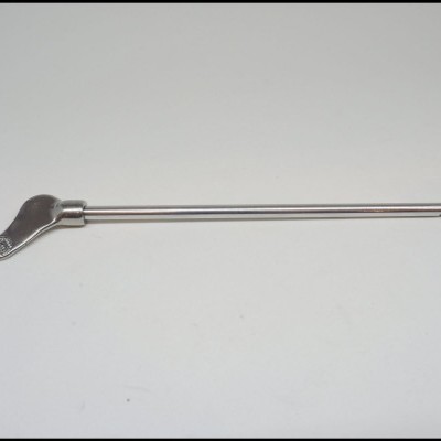 Agulha metálica prateada longa com ponta plana curva sobre superfície branca