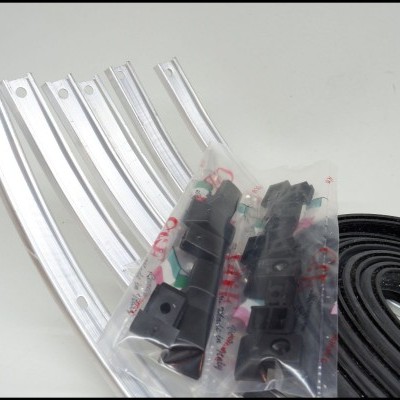 Calhas metálicas curvas prateadas, peças pretas embaladas e tira preta enrolada sobre fundo branco