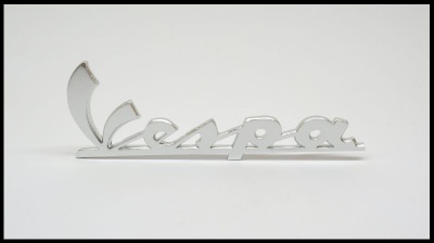 Insígnia metálica prateada com a palavra Vespa