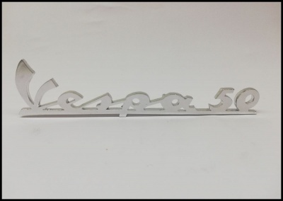 Emblema metálico prateado com texto Vespa 50 em estilo cursivo