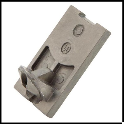 Peça metálica cinzenta rectangular com marcas e relevos sobre fundo branco