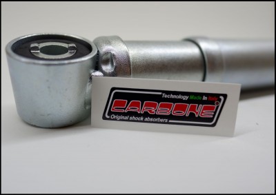 Amortecedor metálico prateado com autocolante 'CARBONE Original shock absorbers' em fundo branco