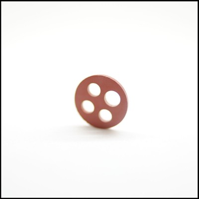 Botão redondo castanho com quatro furos em superfície branca