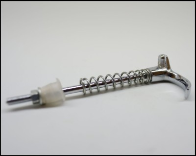 Peça metálica com mola espiral e peça plástica translúcida sobre superfície branca