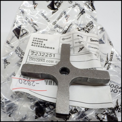 Peça metálica em forma de cruz sobre embalagem com etiquetas e texto