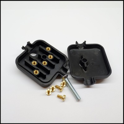 Caixa preta de plástico aberta com insertos metálicos dourados e parafuso prateado em superfície branca