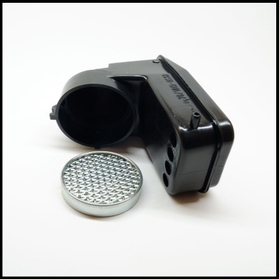 Caixa plástica preta angular com peça circular metálica texturizada sobre fundo branco