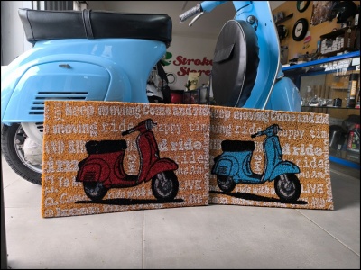 Dois tapetes com desenhos de scooters vermelha e azul numa oficina com scooter azul clara ao fundo