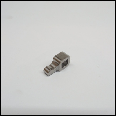 Peça metálica pequena com orifício quadrado sobre fundo branco