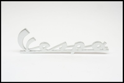 Emblema metálico prateado da palavra Vespa sobre fundo branco