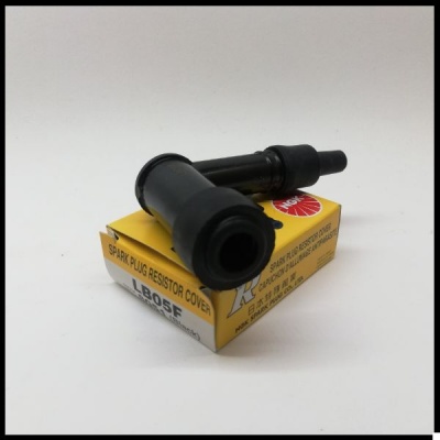 Capa resistora para vela de ignição preta sobre caixa amarela com texto